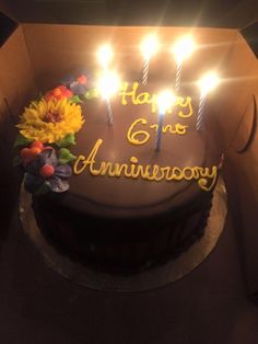 a birthday cake with lit candles and flowers on the top is in a cardboard box