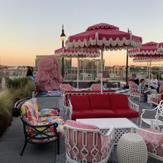 an outdoor seating area with pink and white chairs, umbrellas and tables on the roof