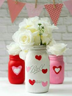 three painted mason jars filled with white and pink flowers on a table next to bunting flags