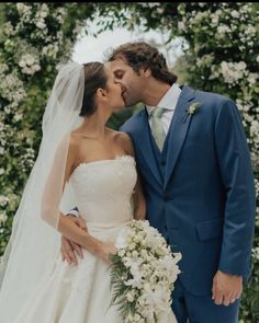 a bride and groom kissing in front of an arch of flowers