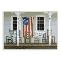 an american flag on the front porch of a white house with rocking chairs in front