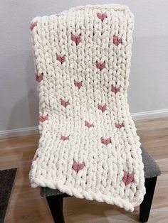 a white crocheted blanket sitting on top of a wooden chair next to a wall