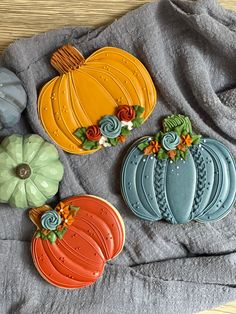 three decorated cookies sitting on top of a gray towel next to pumpkins and flowers