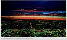 an aerial view of the city at night with colorful clouds in the sky and buildings lit up