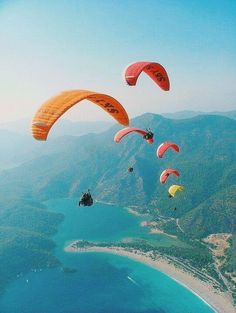 several parasailers are flying over the ocean and mountains