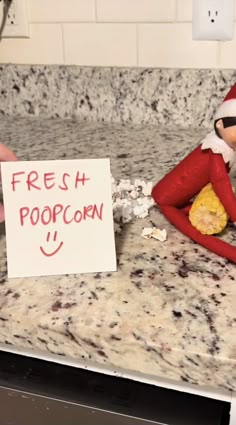 an elf is sitting on the counter with a sign