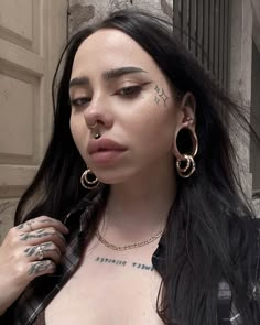 a woman with large hoop earrings and piercings on her face standing in front of a building