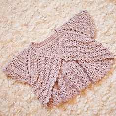 a pink crocheted shawl laying on top of a white carpeted floor