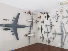 a wall filled with assorted model airplanes on top of wooden floor next to white walls