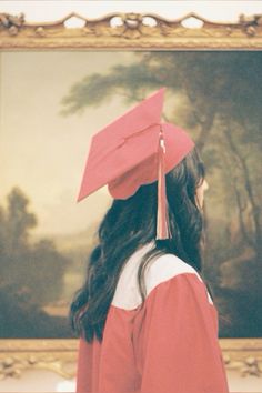 a woman wearing a red cap and gown in front of a painting