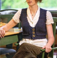 a woman sitting at a table wearing a blue knitted vest with buttons on it