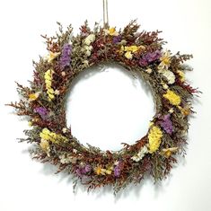 a wreath with dried flowers hanging from a hook on a white wall in the shape of a circle