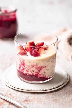 a dessert with strawberries and cream in a glass dish on a plate next to a fork