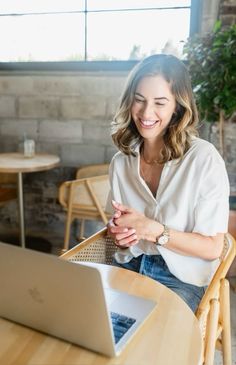 a woman sitting at a table with a laptop computer in front of her and smiling