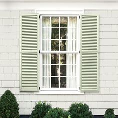 an open window with green shutters in front of a white house