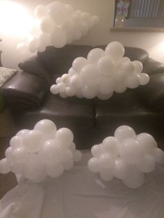 some white balloons are floating in the air on a black leather couch with a light behind it