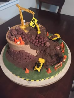 a birthday cake with construction trucks and grapes on it's side, sitting on a table