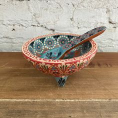 a bowl with spoons in it sitting on a wooden table next to a brick wall