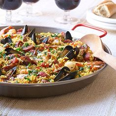 a pan filled with rice and mussels on top of a table next to wine glasses