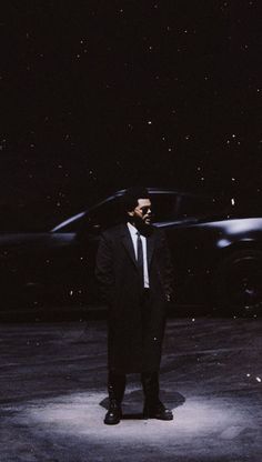 a man in a suit and tie standing next to a black sports car at night