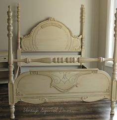 an antique white bed frame with wooden posts and headboard, in front of a window