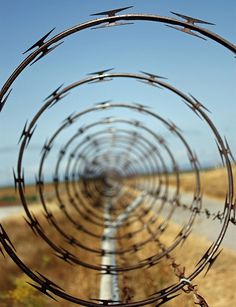 barbed wire is in the middle of an open field with a road and blue sky behind it