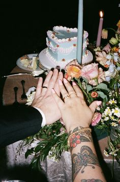 two people reaching for a cake on a table with flowers and candles in the background