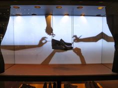 the shadow of two people holding hands in front of a glass display case with shoes on it