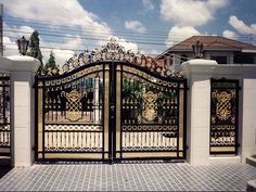 an iron gate in front of a white house with blue sky and clouds behind it