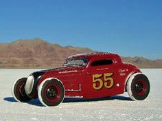 an old red car with numbers painted on it's side in the middle of nowhere