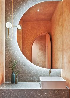 a bathroom sink sitting under a mirror next to a vase with a plant in it