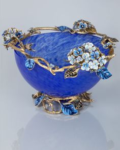 a blue glass bowl with flowers and leaves on the rim, sitting on a reflective surface