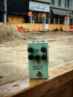 an electric guitar pedal sitting on top of a wooden rail in front of a construction site