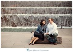 a man and woman sitting on a bench next to a waterfall