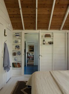 a bed sitting under a wooden ceiling next to a white book shelf filled with books