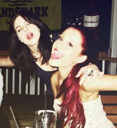 two young women sitting at a table with drinks in front of them and one is sticking her tongue out