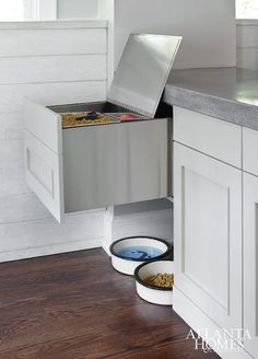 an open cabinet in the corner of a kitchen with two bowls and one bowl on the floor