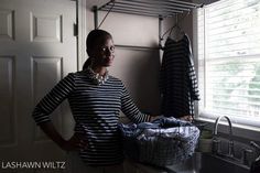 a woman standing in front of a sink next to a drying rack with clothes hanging on it