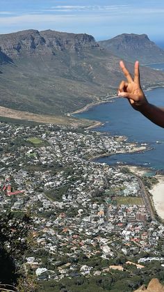 a person making the peace sign with their hand on top of a mountain overlooking a city