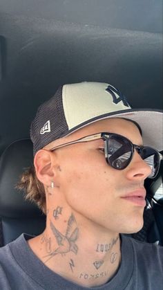 a man wearing sunglasses and a hat with tattoos on his face sitting in a car