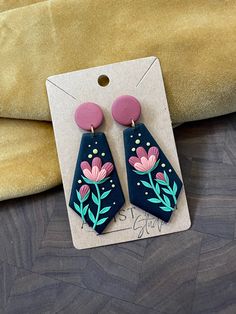 a pair of blue and pink earrings with flowers painted on the front, sitting on a piece of cardboard