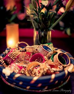 a bowl filled with lots of jewelry next to a vase full of flowers and a lit candle