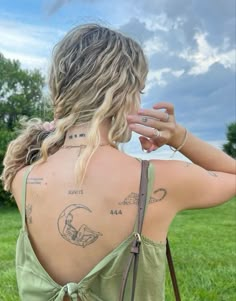 a woman with tattoos on her back standing in the grass