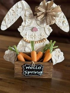 a wooden box filled with carrots sitting on top of a table next to a sign that says hello spring