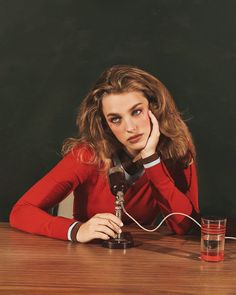 a woman sitting at a table with an old fashioned telephone in her hand and a glass of water next to her