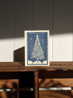 a blue and white christmas tree card sitting on top of a wooden table next to a window