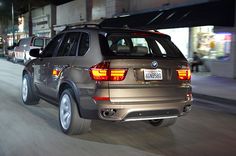 the back end of a silver bmw suv driving down a city street at night with buildings in the background