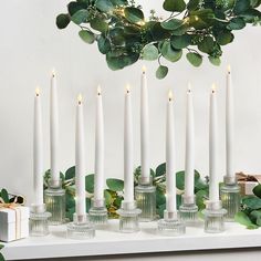 the candles are lined up in rows on the table with greenery around them and one candle is lit