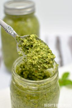 a jar filled with green pestle on top of a white table next to a spoon