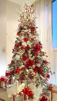 a white christmas tree with red and silver decorations, presents under the tree in front of a window